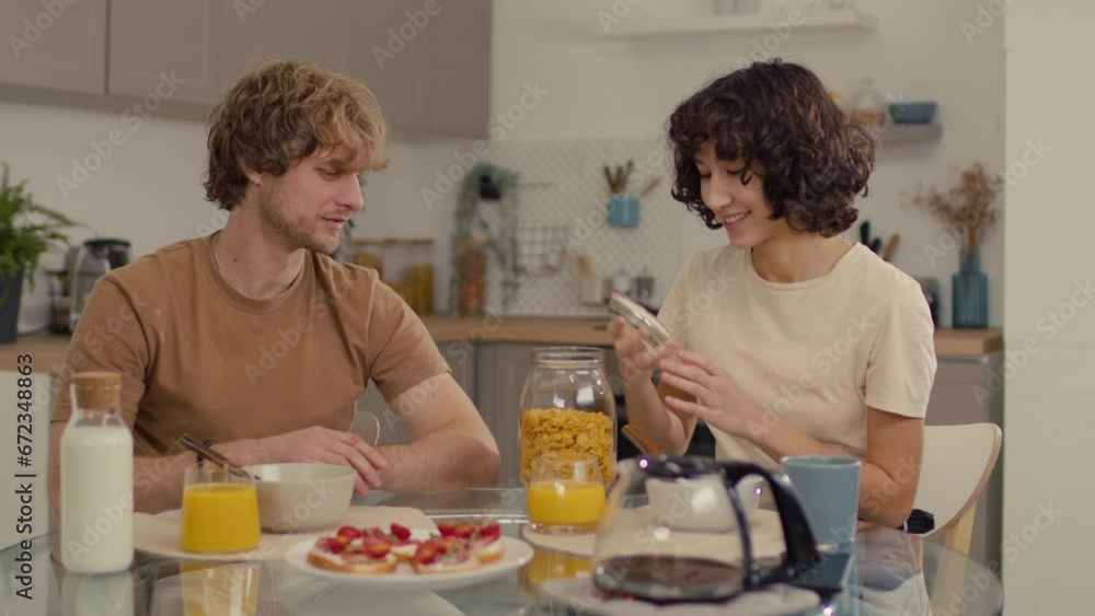 Young couple sitting in kitchen having breakfast made of cereals and sandwiches Young couple sitting in kitchen having breakfast made of cereals and sandwiches