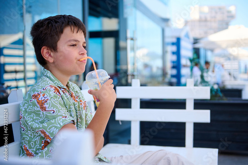 Adorable Hispanic teenage boy drinking healthy smoothie, sitting on a cafe outdoor