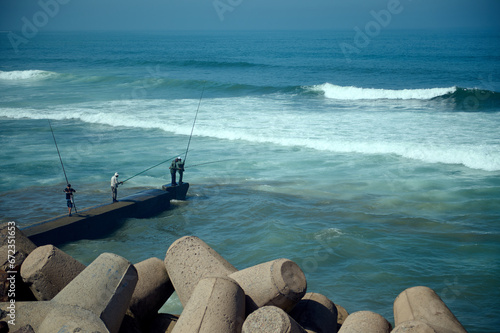 Rear view of unrecognizable people - fisherman standing on the seashore on breakwater and fishing in Atlantic Ocean