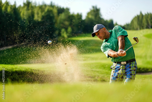 Golfer hits ball from a bunker with golf club photo