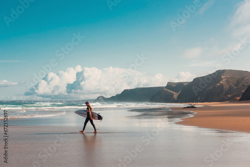 Young female surfer walking into Atlantic Ocean on sandy beach in Portugal