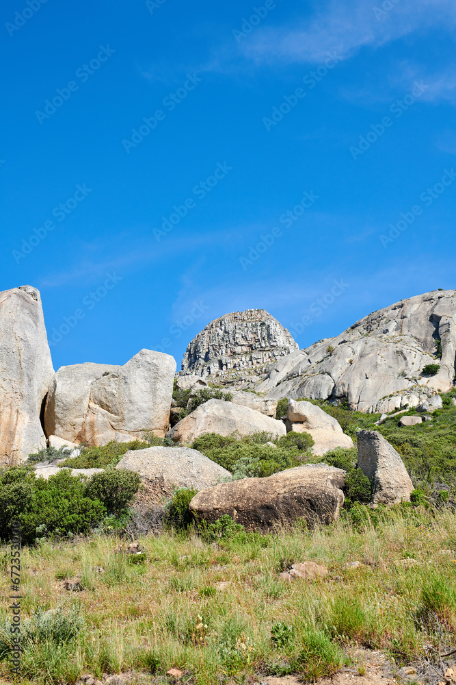Copy space with rocks and boulders in rough hiking terrain with blue sky and copyspace. Lush green grass, wild shrubs and flora growing among stone monolith in a quiet nature reserve or countryside