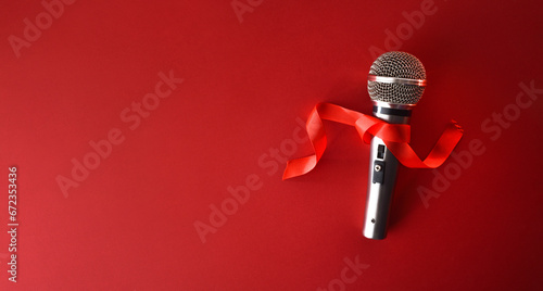 Metal microphone with red bow on red background top view photo