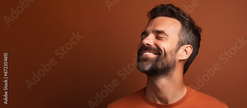 A man with a joyful expression on his face is deep in thought with his eyes shut while surrounded by a brown backdrop