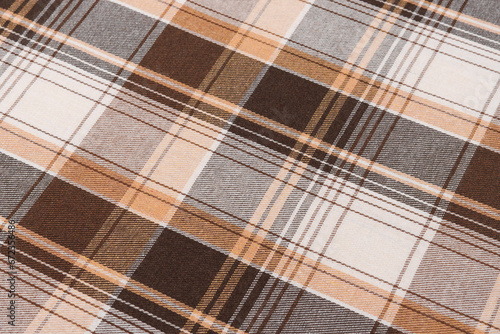 Close-up texture of brown and ivory checked tartan fabric in tilted view. Traditional Scottish clothing. Image for your design