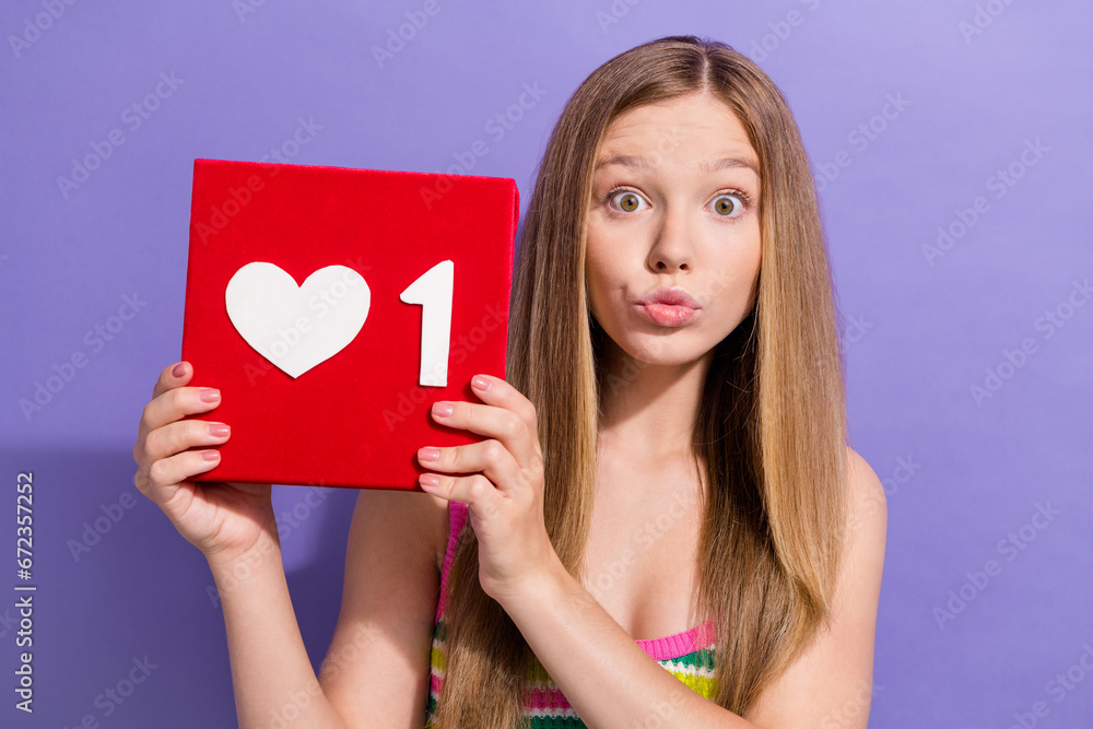 Photo portrait of lovely teen blonde lady hold heart icon pouted lips wear trendy striped garment isolated on purple color background Photo portrait of lovely teen blonde lady hold heart icon pouted lips wear trendy striped garment isolated on purple color background