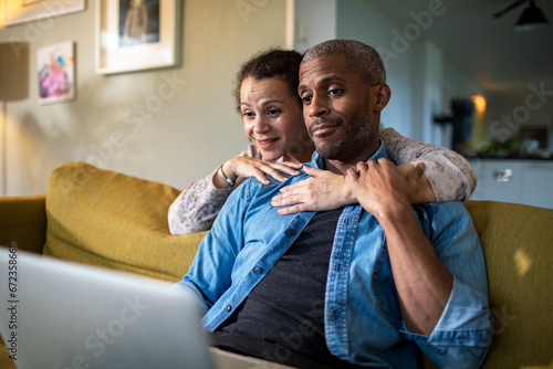 Woman hugging man looking at the laptop together at home photo
