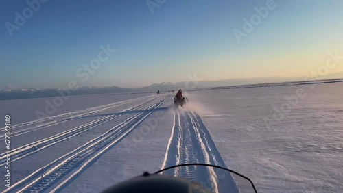 First Person Shooting. A man in a red jacket on a snowmobile quickly rides along the winter snowy Lake Baikal at high speed. Tourists and winter active recreation. Cloudy weather. Blue sky