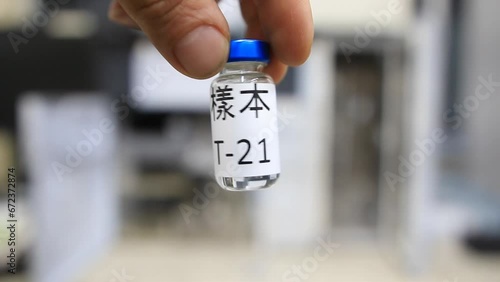 A close up from a man holding a vial with a liquid labelled as sample in chinese characters inside a analytical chemistry laboratory photo