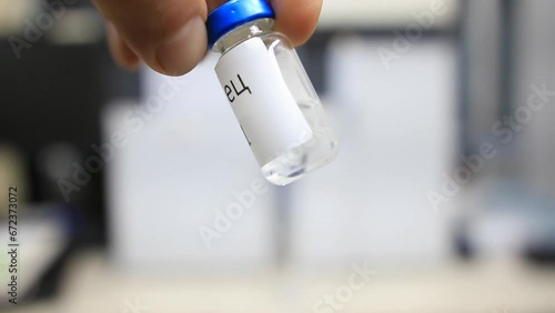 A man holding a vial with a liquid labelled as sample in russian characters inside a analytical chemistry laboratory photo