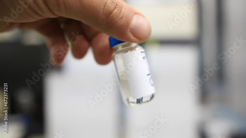 A close up from a man holding a vial with a liquid labelled as sample in hindi inside a analytical chemistry laboratory photo