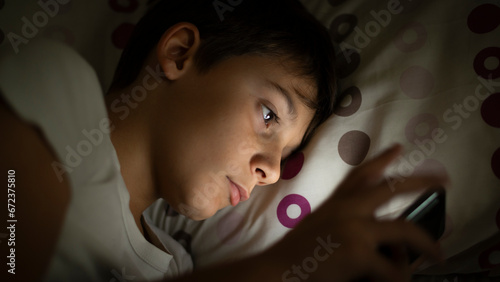 Child inside social networks with his smartphone from bed at night before sleeping. Concept of kids using social networks and their dangers without parental control at night from their room photo