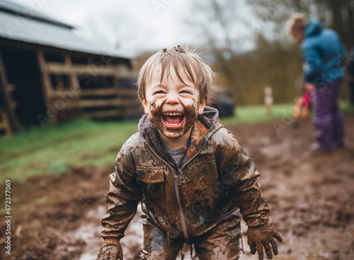 A little boy squeals with delight after getting soaked with mud, playing on a farm laughing and giggling, being a kid, covered in mud from head to toe