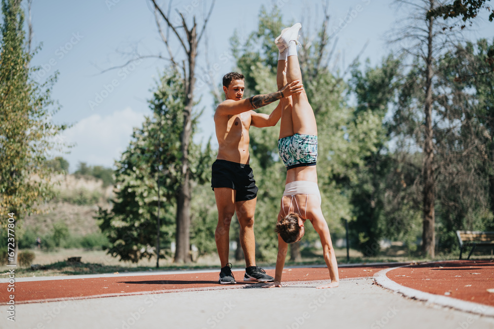 Obraz premium Active couple practices handstands in a sunny park, showcasing fit bodies and strong muscles. They enjoy outdoor training, embracing the natural environment and positive results of physical activity.