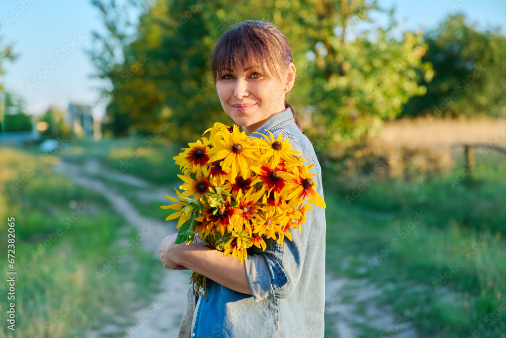 Happy middle aged woman with bouquet looking at camera, rural nature Happy middle aged woman with bouquet looking at camera, rural nature