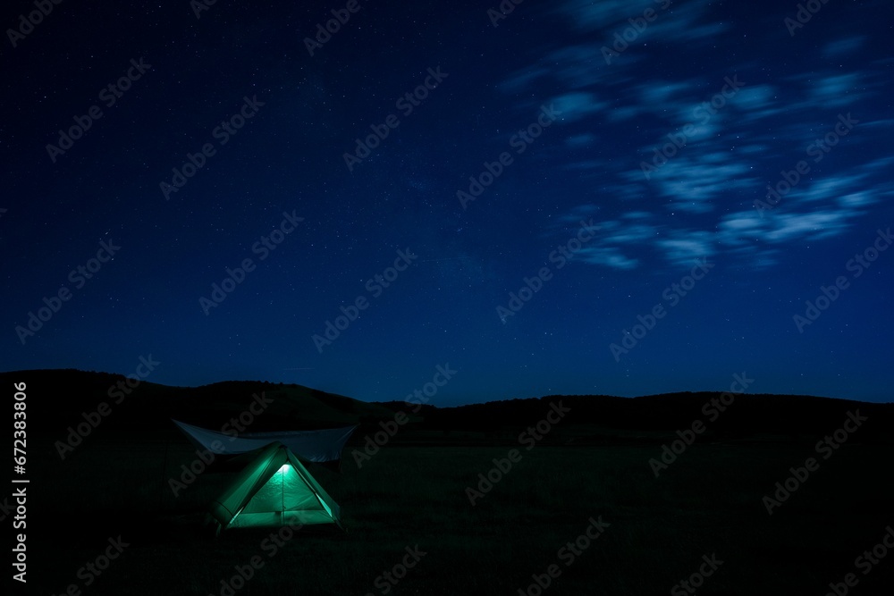 Cozy camping tent illuminated by the soft glow of the stars in a vast grassy landscape