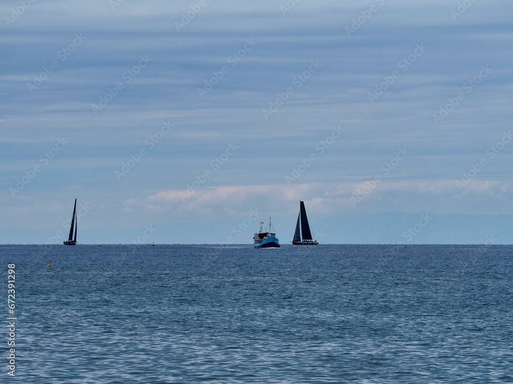 Sailboats float in the middle of a serene sea against a clear blue sky