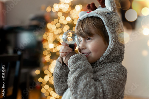 A little boy in a warm pajamas plays with a prism ball against the backdrop of Christmas lights. Magical home New Year with children. . High quality photo
