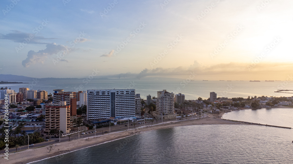 Drone photos of the City of Lechería on a sunset, in which you can see buildings, sea, people bathing on the beach, and passers-by.
Playa los Canales Boulevard