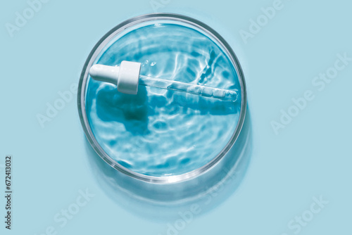 Liquid pipette serum blue gel on light cyan colored Petri dish background