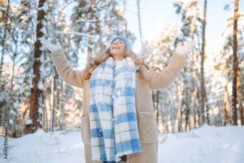 A young woman throws out snow. Portrait of a happy woman playing with snow on a sunny winter day. A walk through the winter forest. Concept of fun, relaxation.
