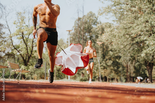 Active caucasian couple running together in the park, training outdoors with a parachute for better body shape and power. Their fit bodies showcase the positive results of their workout.