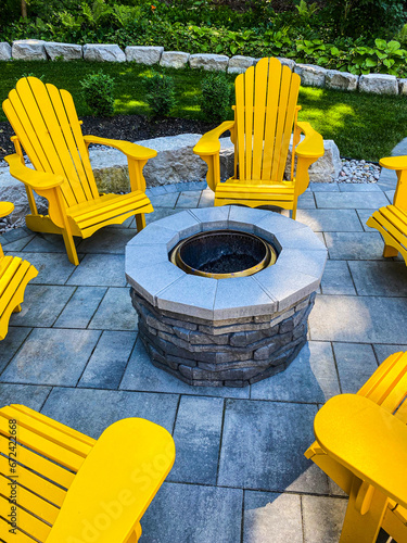 Yellow Muskoka chairs in a circle around a beautiful stone fire pit in estate residential backyard in summer.