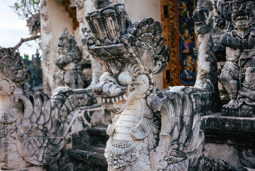 Detailed close-up of a mythical balinese dragon statue, surrounded by other stone figures, set against the backdrop of an ornate temple entrance
