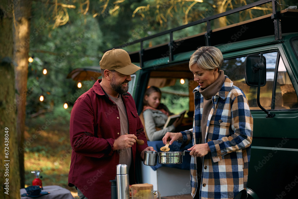 Happy parents cooking during family camping trip in woods. - obrazy, fototapety, plakaty 