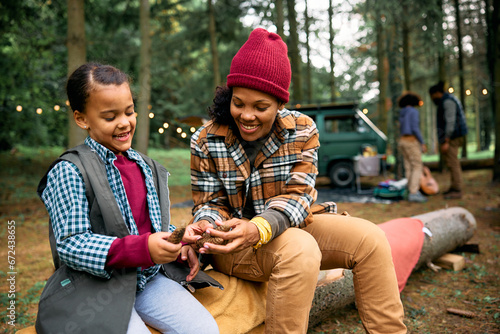 Happy black mother and daughter playing with pine cones while camping in woods. © Drazen