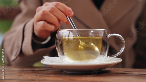 Woman stirs green tea with spoon in glass cup on table in cafe of park