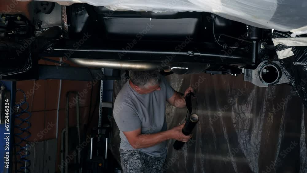 A worker wraps the elements of the bottom of the car with stretch film. A worker wraps the elements of the bottom of the car with stretch film.