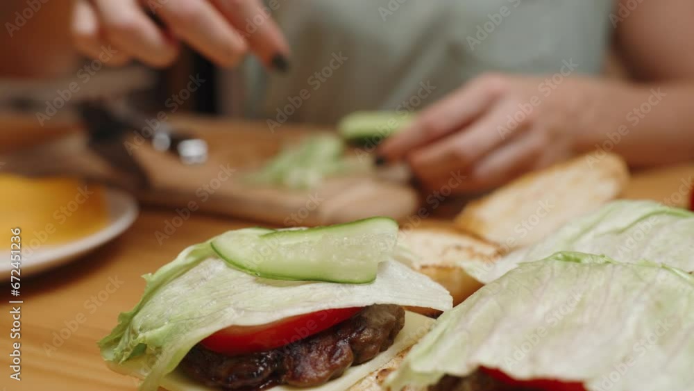 Burgers in a Homey Setting, a Woman Places Cucumber Slices on Top, Ingredients for Preparation. Burgers in a Homey Setting, a Woman Places Cucumber Slices on Top, Ingredients for Preparation.