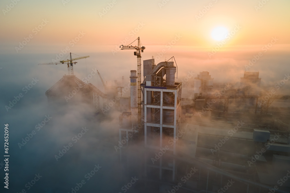 Aerial view of cement factory with high concrete plant structure and tower crane at industrial production site on foggy morning. Manufacture and global industry concept