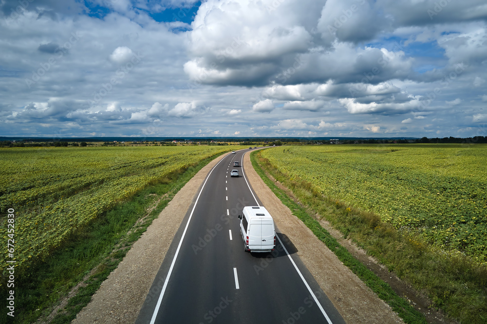 Fototapeta premium Aerial view of intercity road between green agricultural fields with fast driving cars. Top view from drone of highway traffic