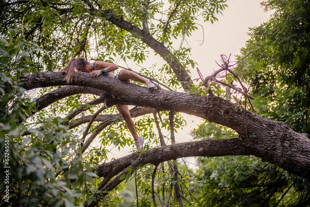 A fit, athletic woman climbs a tree in a green park, exercising and warming up her body. She enjoys a sporty and active lifestyle, training outdoors in nature. A fit, athletic woman climbs a tree in a green park, exercising and warming up her body. She enjoys a sporty and active lifestyle, training outdoors in nature.