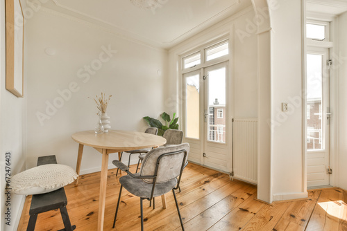 a dining table and chairs in a room with white walls, hardwood flooring and large windows looking out onto the street