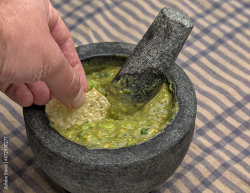 hand dipping tortilla chip into guacamole inside molcajete (traditional mexican mortar and pestle for grinding spices and making sauces) spicy avocado dip with aztec roots (man, white, caucasian)