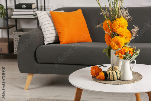 Fotografi Beautiful autumn bouquets and pumpkins on coffee table near sofa in room