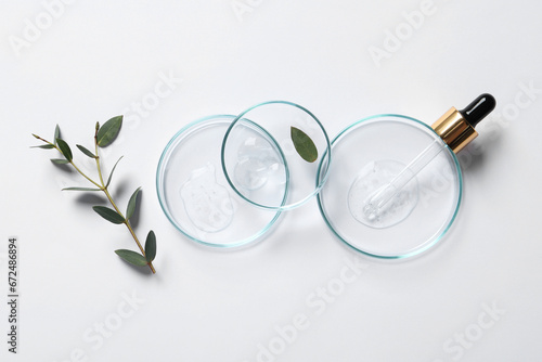 Petri dishes with samples of cosmetic oil, pipette and green leaves on white background, flat lay
