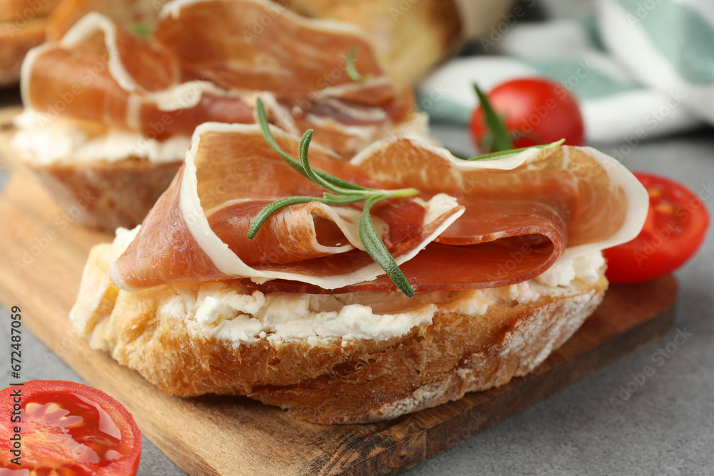 Tasty sandwiches with cured ham, tomatoes and rosemary on grey table, closeup
