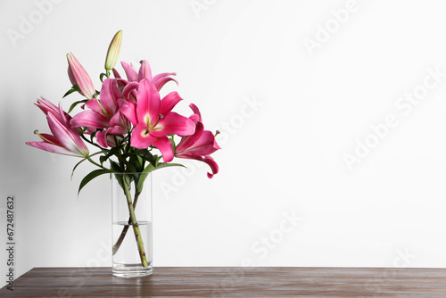 Fototapeta Naklejka Na Ścianę i Meble -  Beautiful pink lily flowers in vase on wooden table against white background, space for text