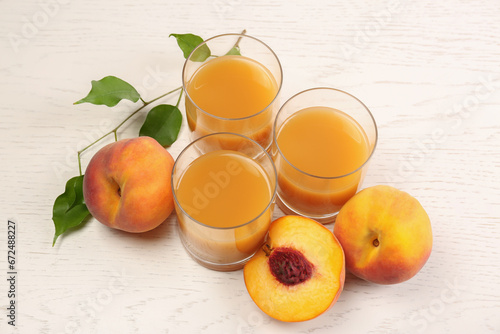 Glasses of delicious peach juice, fresh fruits and leaves on white wooden table, above view