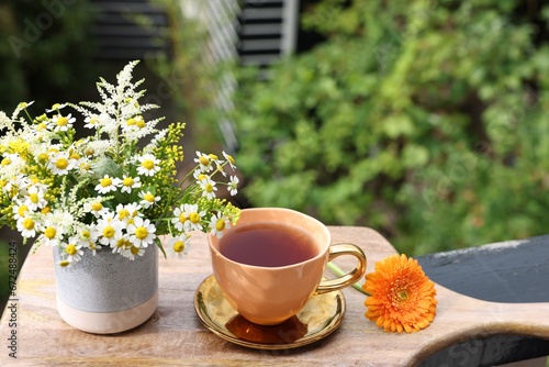 Cup of delicious chamomile tea and fresh flowers outdoors on sunny day. Space for text