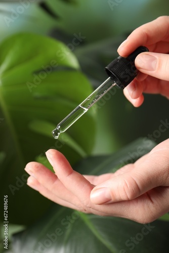 Woman applying cosmetic serum onto finger on green background  closeup