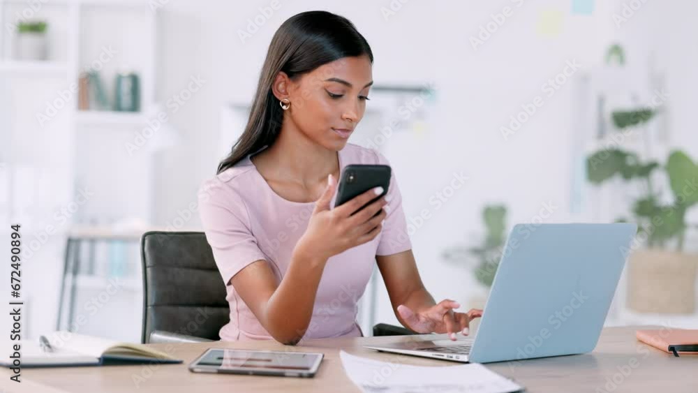 Business analyst typing on laptop, reading data from phone, updating data charts online. Confident, ambitious and multitasking professional sitting alone in office, connected to technology Business analyst typing on laptop, reading data from phone, updating data charts online. Confident, ambitious and multitasking professional sitting alone in office, connected to technology