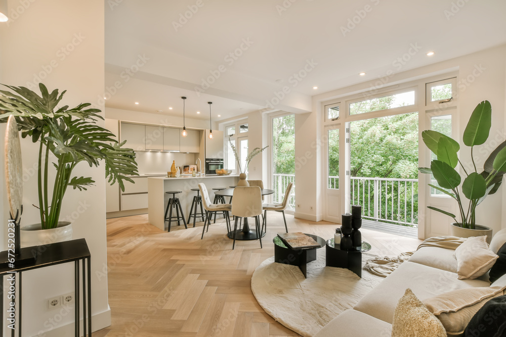 a living room with wood flooring and white walls that are open to the kitchen, dining area and balcony - obrazy, fototapety, plakaty 