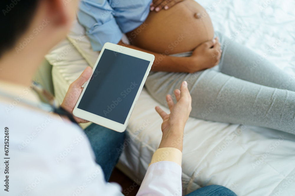 Asian male doctor visit to African - American pregnant woman patient home to talk and check for pregnancy health. On site - home medical service concept.