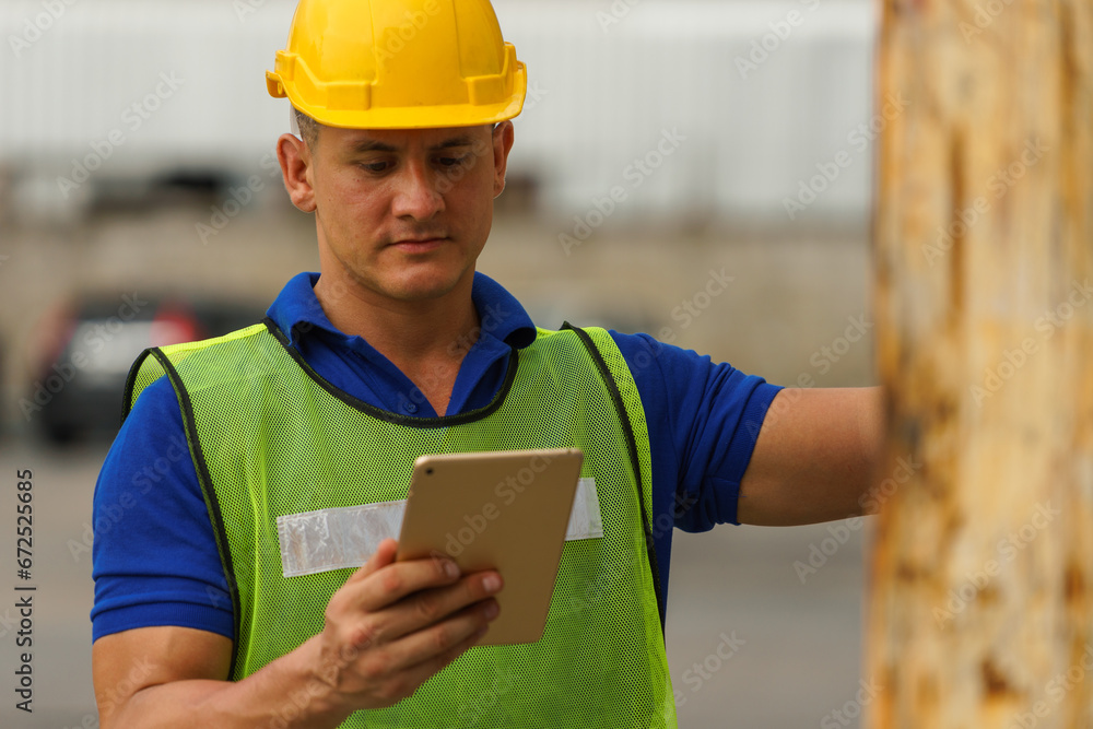 Caucasian man wearing yellow safety helmet Carrying a genuine tablet to check electrical equipment In the container storage yard Caucasian man wearing yellow safety helmet Carrying a genuine tablet to check electrical equipment In the container storage yard