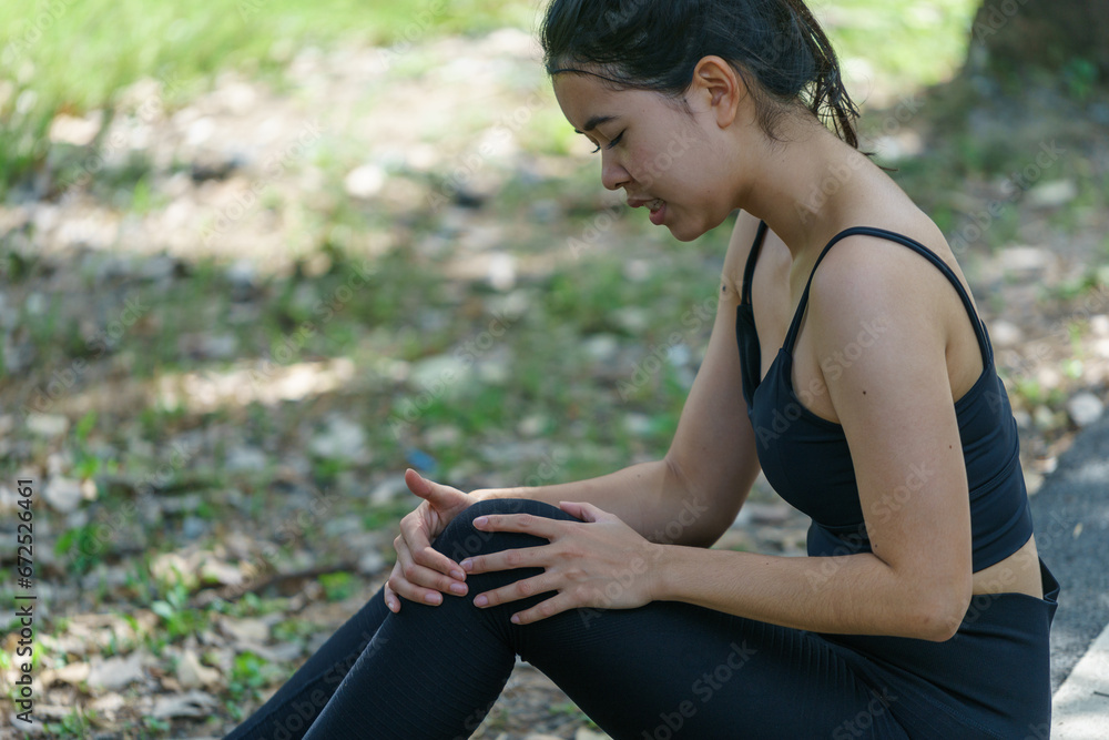 Young Asian woman wearing black exercise clothes Sitting hurts knees and legs After exercising in the park Young Asian woman wearing black exercise clothes Sitting hurts knees and legs After exercising in the park